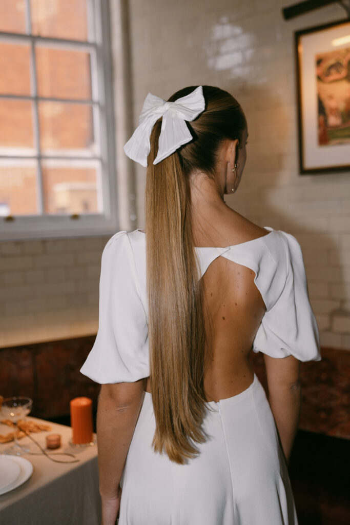 Stylish bride with a sleek ponytail with a big white bow and bridal dress