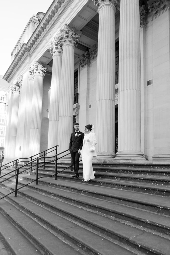 black and white wedding photo of newlyweds walking down the stairs together outside old marylebone town hall